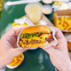 Hands holding cheeseburger over fast food meal